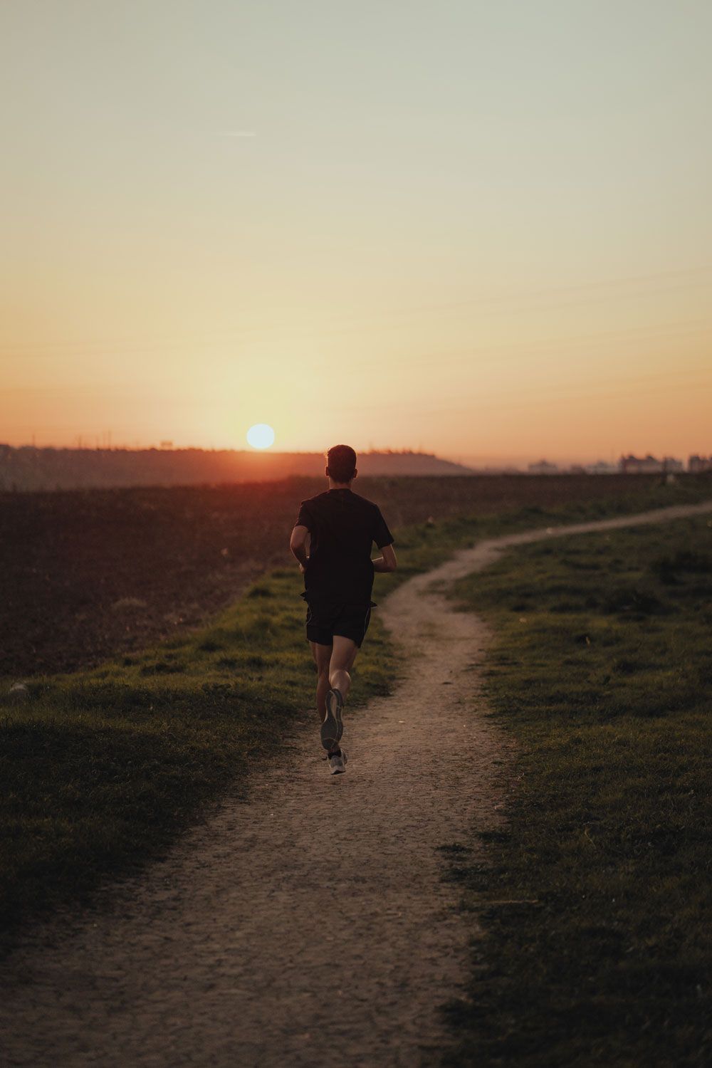 Alex Quijada sale a correr solo por un sendero de tierra que atraviesa campos abiertos al atardecer, con el sol ya bajo en el horizonte y el cielo teñido de naranja.